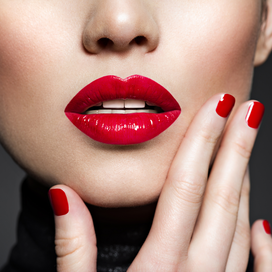 women's half face image with red painted nails touching chin with bright red lipstick